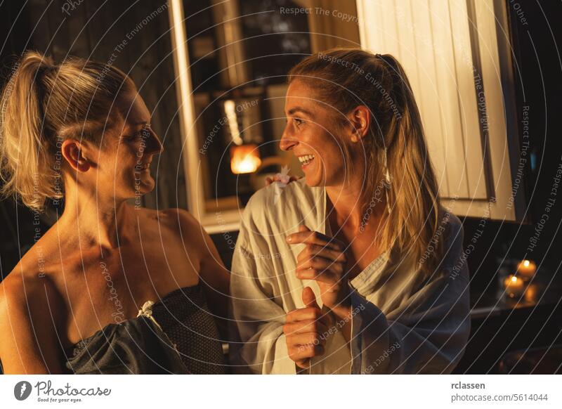 Two smiling women sitting at the entrance of a Finnish barrel sauna, enjoying the moment. mobile hotel finnish sauna relaxation wellness spa friends enjoyment