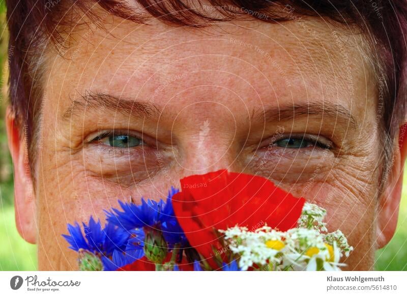 Summer. (M)A young woman smiles into the camera from behind a bouquet of field flowers. portrait Woman Young woman Face Feminine pretty Hair and hairstyles