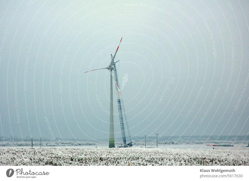 Gigantic. A wind turbine is being erected. The true size only becomes apparent when compared with the electricity pylons and the forest in the background, and the snow and ice give an idea of how laborious it is to erect such objects.