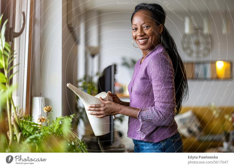 Beautiful woman watering plants at home people joy black natural attractive black woman happiness happy real people mature adult daily life adults one person