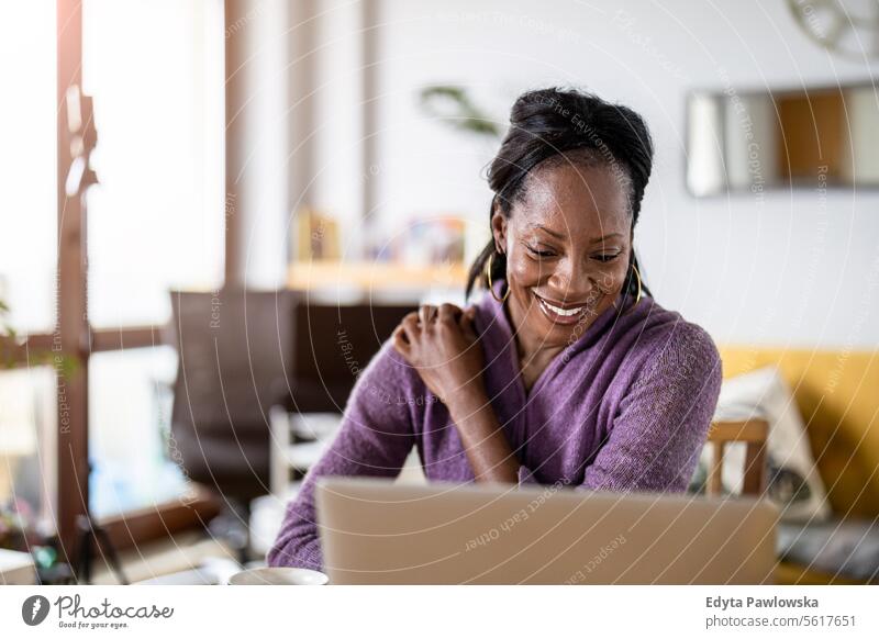 Smiling woman working on laptop at home people joy black natural attractive black woman happiness happy real people mature adult daily life adults one person