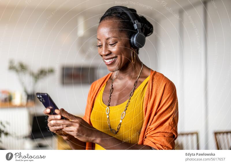 Woman listening to music with headphones connected to her smartphone in the living room at home people joy woman black natural attractive black woman happiness