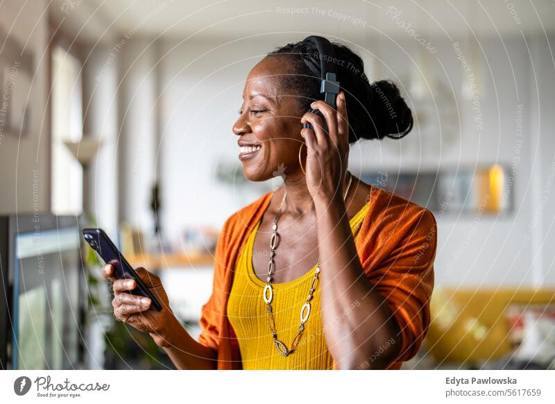 Woman listening to music with headphones connected to her smartphone in the living room at home people joy woman black natural attractive black woman happiness