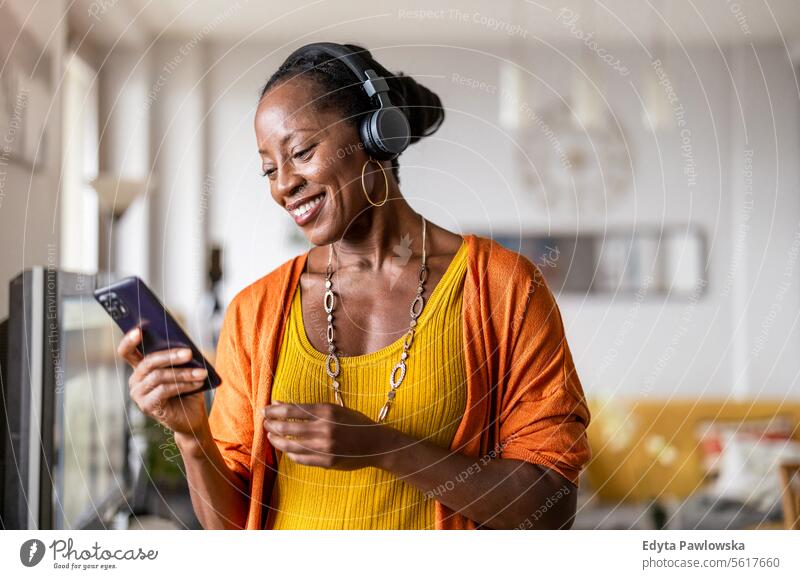 Woman listening to music with headphones connected to her smartphone in the living room at home people joy woman black natural attractive black woman happiness