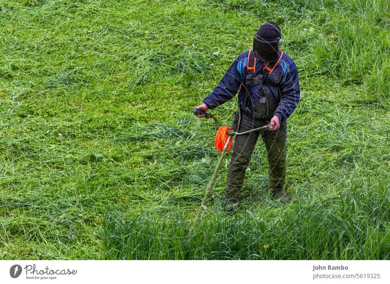 lawnmower man with string trimmer and face mask trimmong grass - close-up protective engine green selective focus mowing public official service work dirty