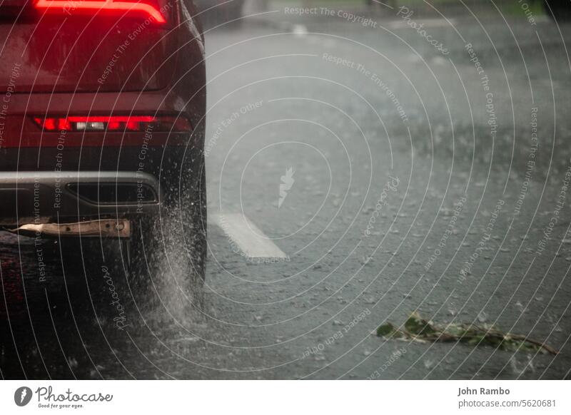 Rain water splash flow from wheels of red car moving fast in daylight city with selective focus. asphalt road during heavy summer storm rain extreme civil