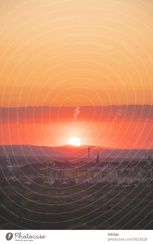 Disc of sunset with reddish hues sets behind the mountains in the distance. Blue, orange and golden sky. Airplane flying over in red sun. Abstract sky freedom