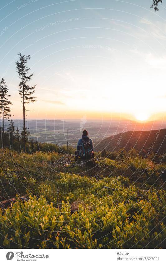 Adventurer sitting on a stump on top of a mountain watching an orange-red sunset. Enjoying success. Beskydy mountains, Czech Republic backpacker freedom dawn