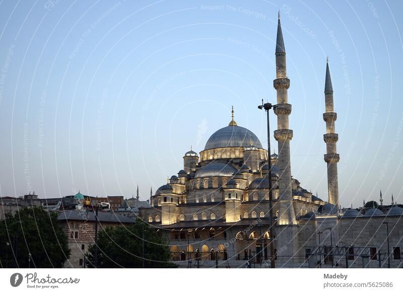 The illuminated Yeni Cami or New Mosque with dome and minaret in the evening at the Galata Bridge on the Golden Horn in the Eminönü district of Istanbul on the Bosporus in Turkey