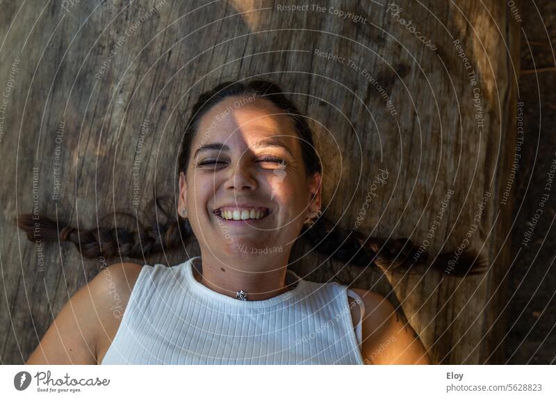 smiling young woman, close-up of a brunette woman with two braids, smiling with her eyes closed lying on a wooden log Smiling Adults 18 - 30 years Young woman