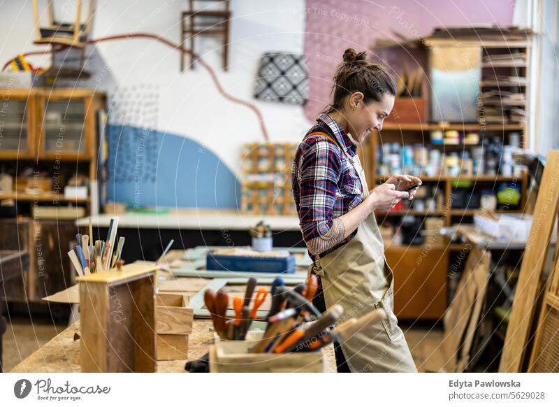 Portrait of young female carpenter using mobile phone in her workshop Furniture Carpenter Restoring Carpentry wood Chair building Manufacturing Craft Renovation