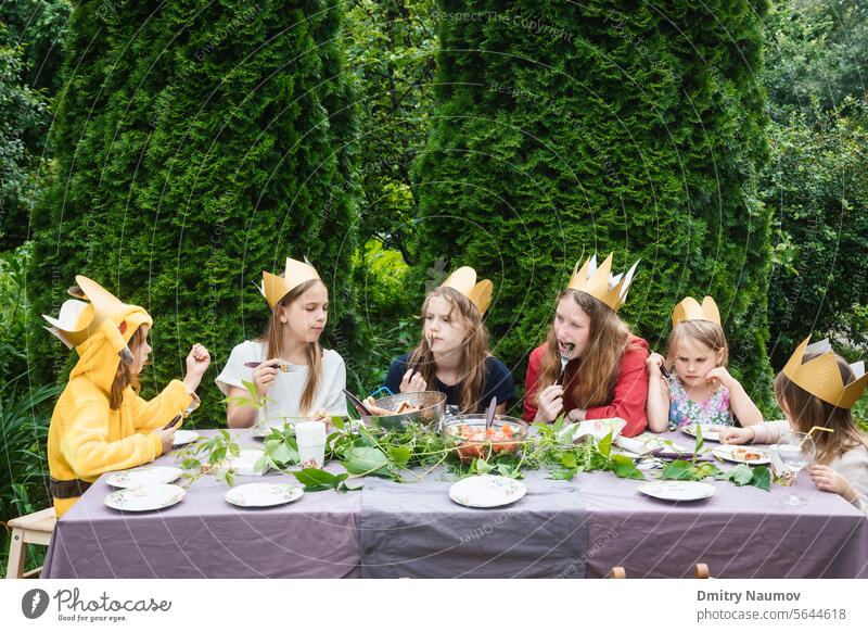 Children having birthday party in green garden anniversary backyard candid caucasian celebrate celebrating celebration child childhood children costume crown