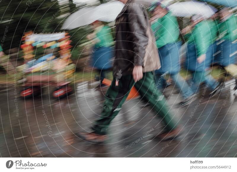 Procession of blurry people in the rain with handcart Group Handcart relocation Cabbage run Carnival street parade Rain Umbrella Bad weather celebrations