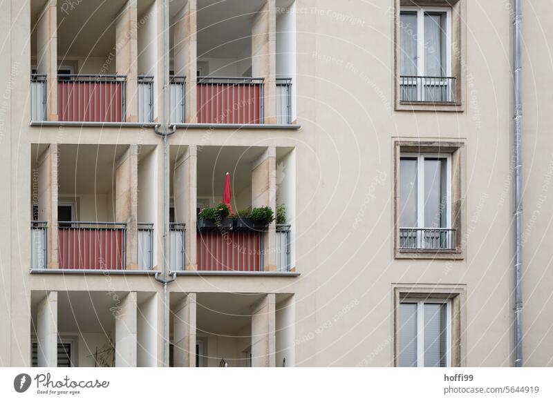 gray residential building façade with red balconies and a folded-in red parasol Apartment Building tenement Balconies 1960s Sunshade Covered dreariness Gloomy