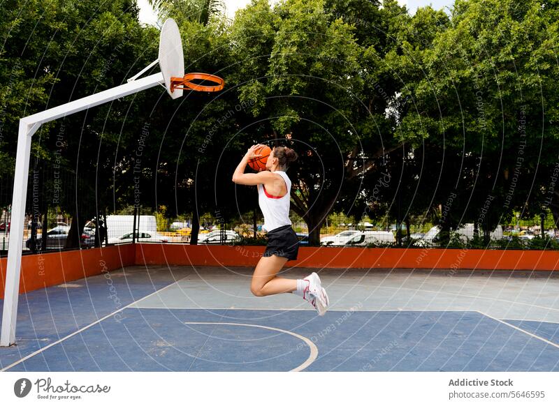 Full length side view of determined young female in sportswear jumping and throwing ball to make basket while playing on court Sportswoman Basketball Throw Jump