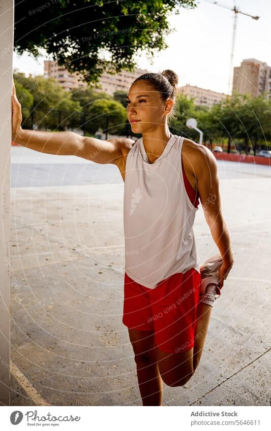 Side view of confident focused fit woman in sportswear standing near post doing warmup exercise before playing basketball on court Sportswoman Stretch Exercise