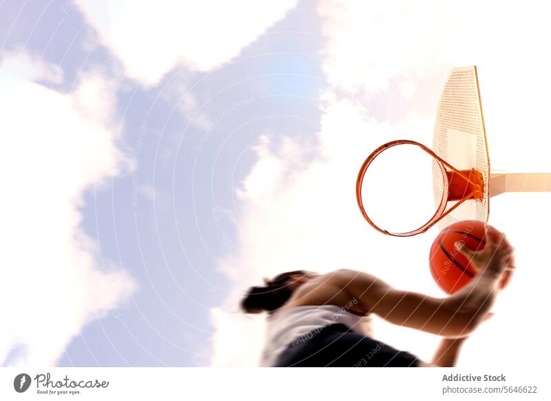 From below of cropped unrecognizable female basketball player in activewear jumping and throwing ball into basket hoop against cloudy sky Sportswoman Basketball