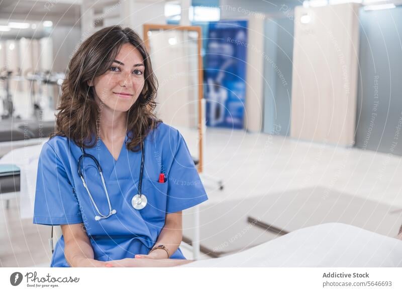 Happy young woman doctor in uniform sitting at table in hospital smile professional stethoscope work health care job female happy pen wristwatch therapist