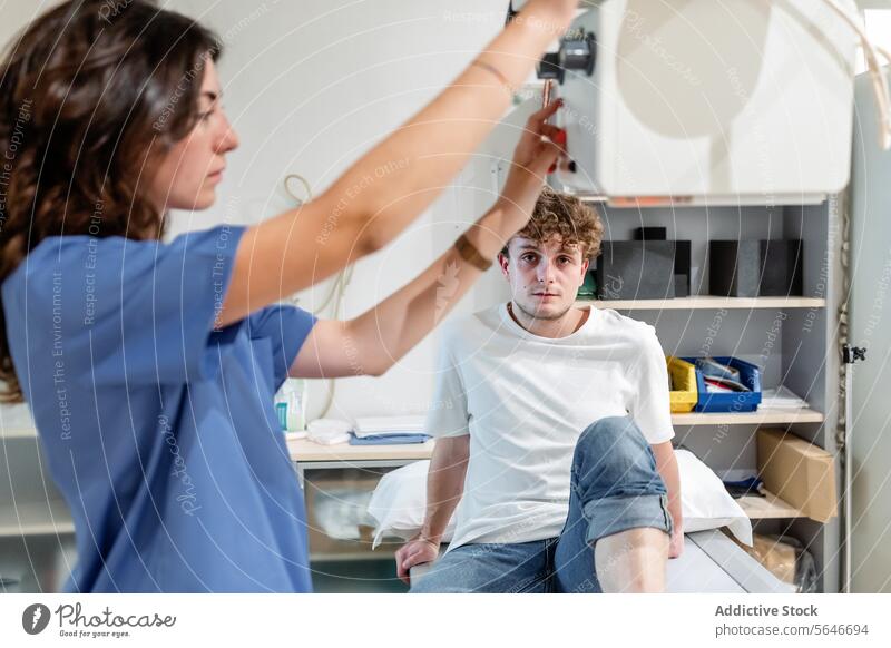 Young female technician adjusts X Ray machine for scanning patient sitting on bed in clinic woman nurse x ray hospital diagnosis health care medicine