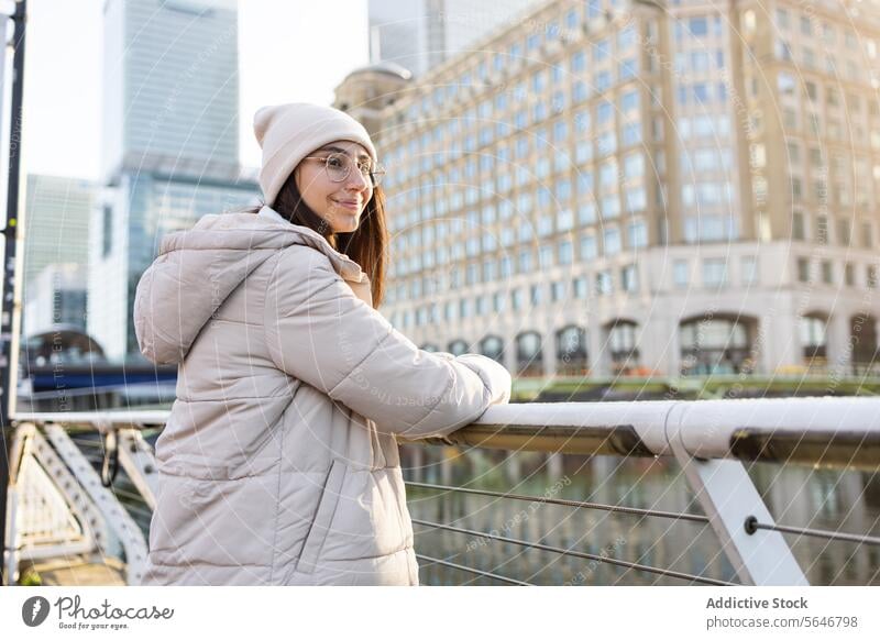 Smiling woman in cozy jacket standing and resting hands on metallic railing street bench building modern warm clothes positive cheerful female urban smile glad