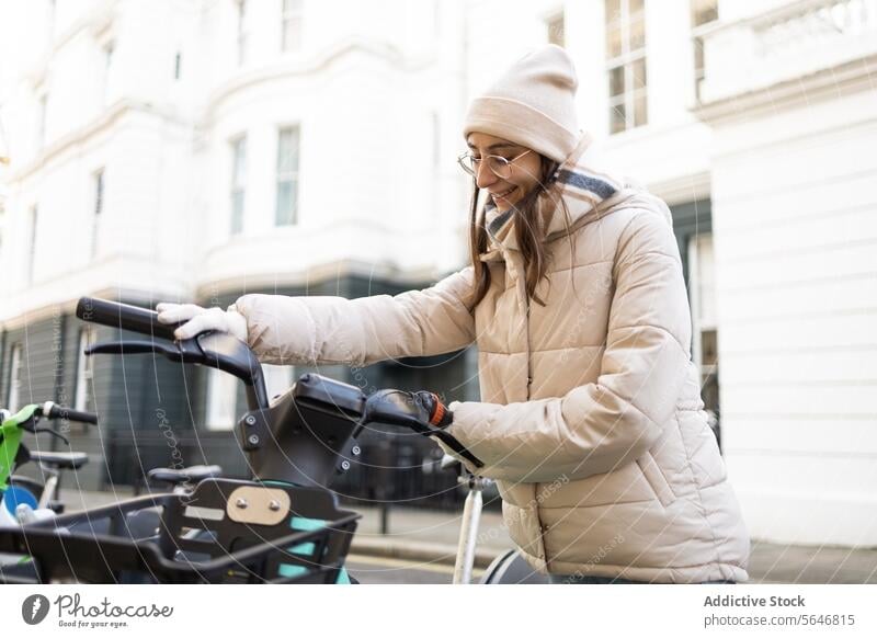 Smiling woman in cozy jacket holding electric bicycle on street scooter city modern building trendy positive warm clothes style smile female facade exterior