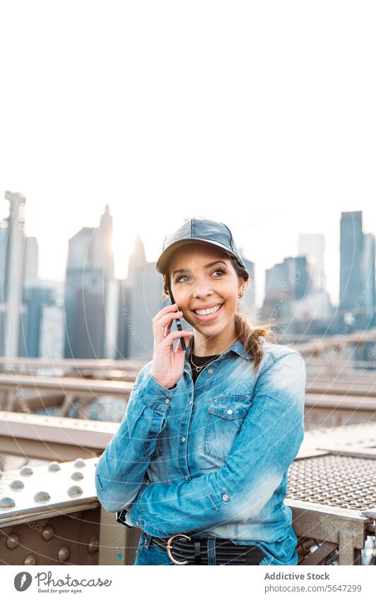 Woman chatting on phone against Manhattan view woman call sunglasses skyline cityscape New York conversation urban bridge fashion joy denim glow lifestyle