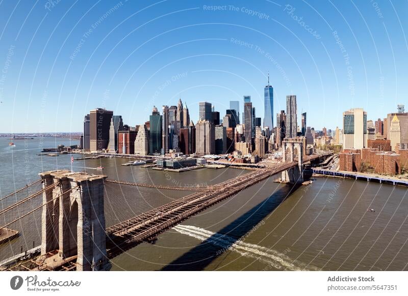 Brooklyn Bridge with city skyline backdrop under blue sky. bridge river New York aerial view architecture landmark buildings towers urban USA skyscrapers