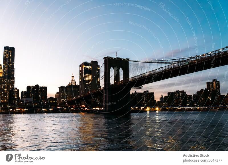 Brooklyn Bridge over river against city in evening cityscape bridge district Brooklyn bridge building skyscraper megapolis tower high rise riverside landmark