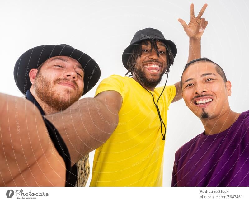 Three friends taking a playful selfie together friendship men young adult cheerful smile happy pose camera peace sign white background casual joy fun