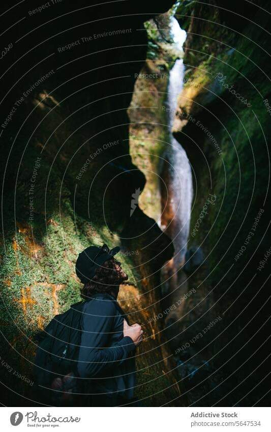 Explorer admires a hidden waterfall in a mossy canyon in Sombrio Beach explorer nature awe person hat gaze secluded vancouver island british columbia canada