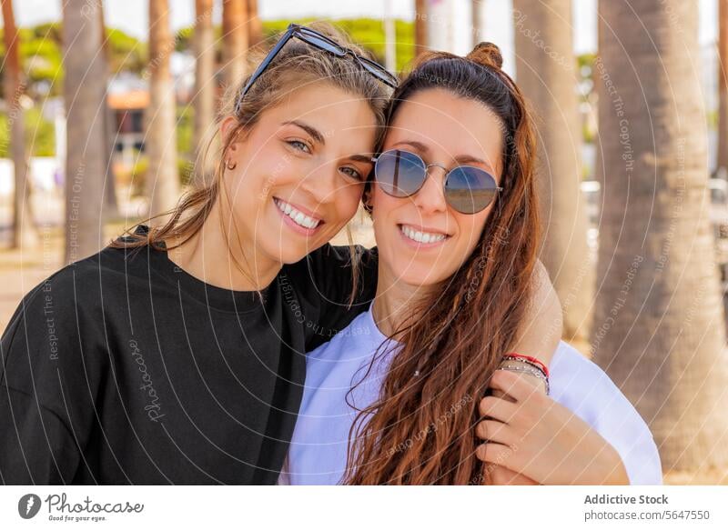 Smiling Caucasian female friends with sunglasses women portrait happy park together fashionable bonding headshot blur arm around smiling brunette blond cheerful