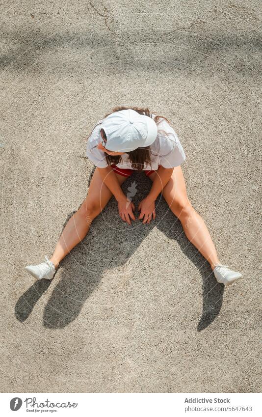 Young woman sitting on pavement, viewed from above aerial view from above shadow rest head on knees sunny outdoor young adult sidewalk city life urban