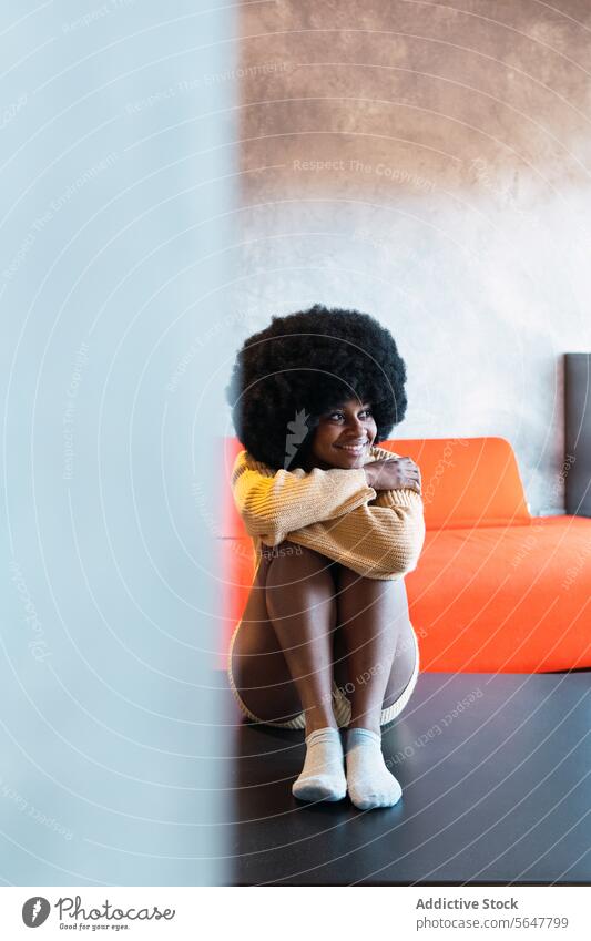 Black woman sitting on floor embracing knees home weekend smile enjoy appearance afro relax personality female black african american young happy curly hair