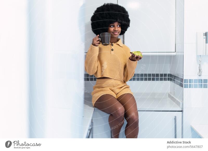 Cheerful black woman sitting at kitchen breakfast morning avocado home relax drink counter enjoy female african american afro curly hair food hot drink toast