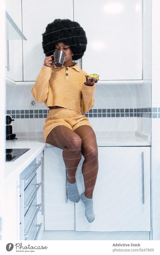 Cheerful black woman sitting at kitchen breakfast morning avocado home relax drink counter enjoy female african american afro curly hair food hot drink toast