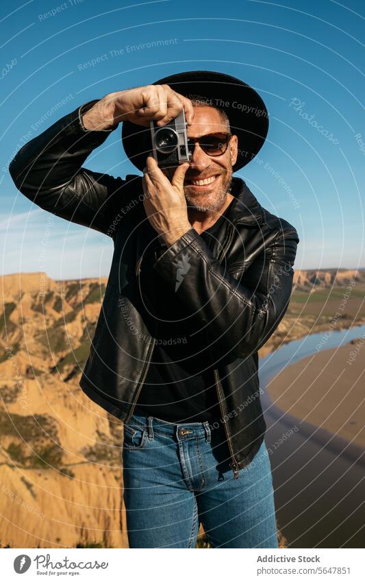 Stylish cheerful photographer taking photos outdoors with analog camera man happy vintage stylish hat leather jacket hobby leisure adventure travel nature