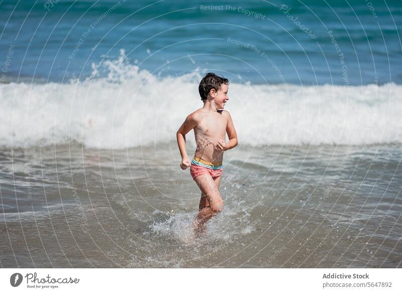 Young boy playing happily in the sea waves child beach splash run joy summer sunny coast ocean happy swimwear vacation leisure fun water playtime seaside shore