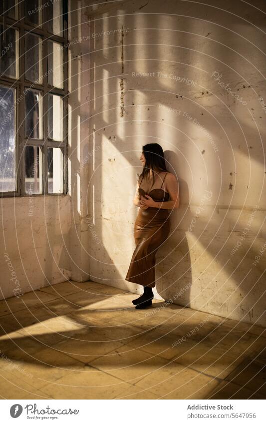 Contemplative woman in sunlit room by a window sunlight shadow contemplation serene indoor standing warm light pensive quiet alone solitude peaceful thoughtful