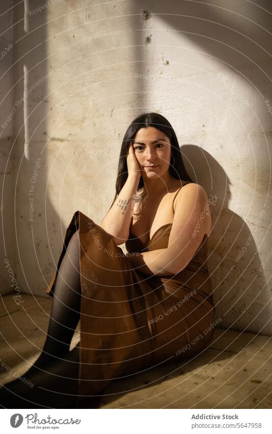 Elegant woman sitting in sunlight with a thoughtful gaze shadow wall dress elegant pensive chic young mood dramatic thinking reflection calm serene indoor