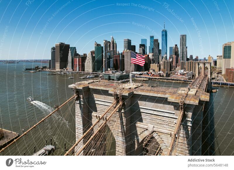 Brooklyn Bridge with city skyline backdrop under blue sky. bridge river New York aerial view architecture landmark buildings towers urban USA skyscrapers