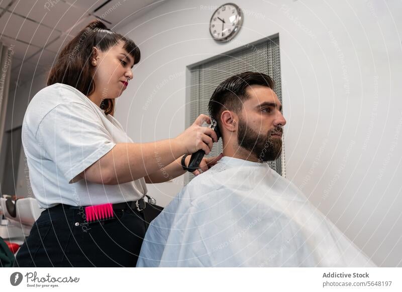 Side view of female hairstylist using electric trimmer on male client's hair at salon Hairdresser Trimmer Man Salon Care Service Hand Client Process Tool