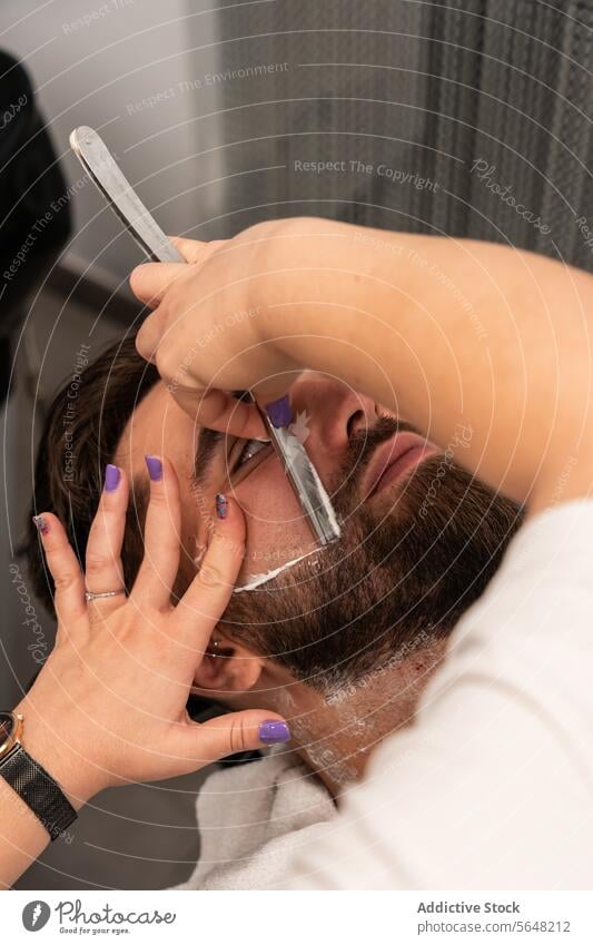 From above crop unrecognizable hands of female barber shaving male client's beard with straight razor at salon Hairdresser Shave Straight Razor Beard Man Salon