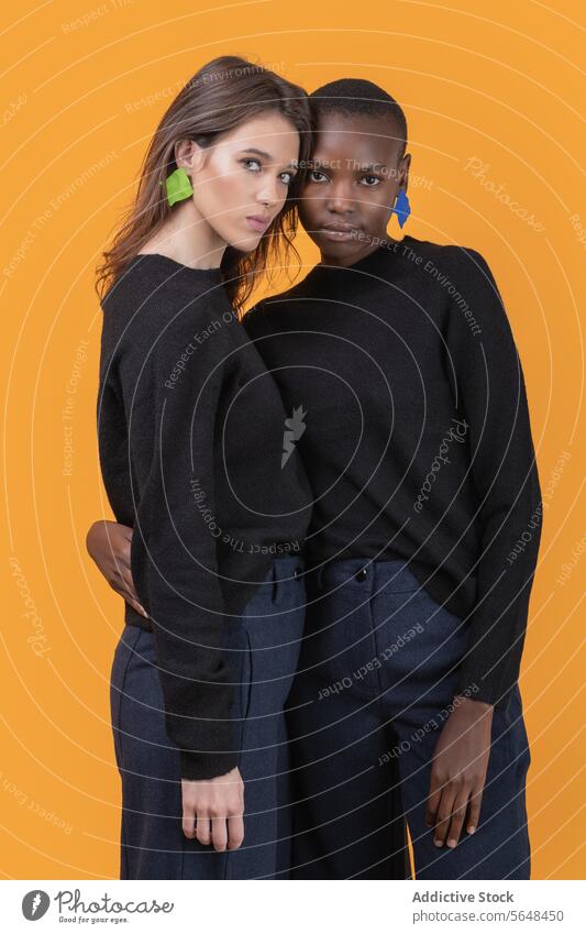 Diverse young female friends wearing pink earrings embracing each other against yellow background women diverse confident portrait trendy tshirt together