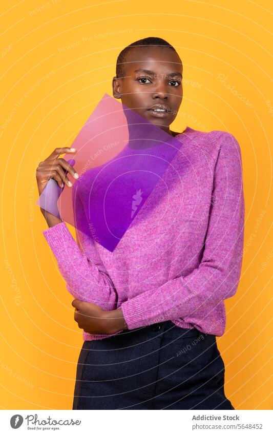 Black woman in warm clothing holding transparent plastic on yellow background purple sweater isolated african american copy space portrait advertisement