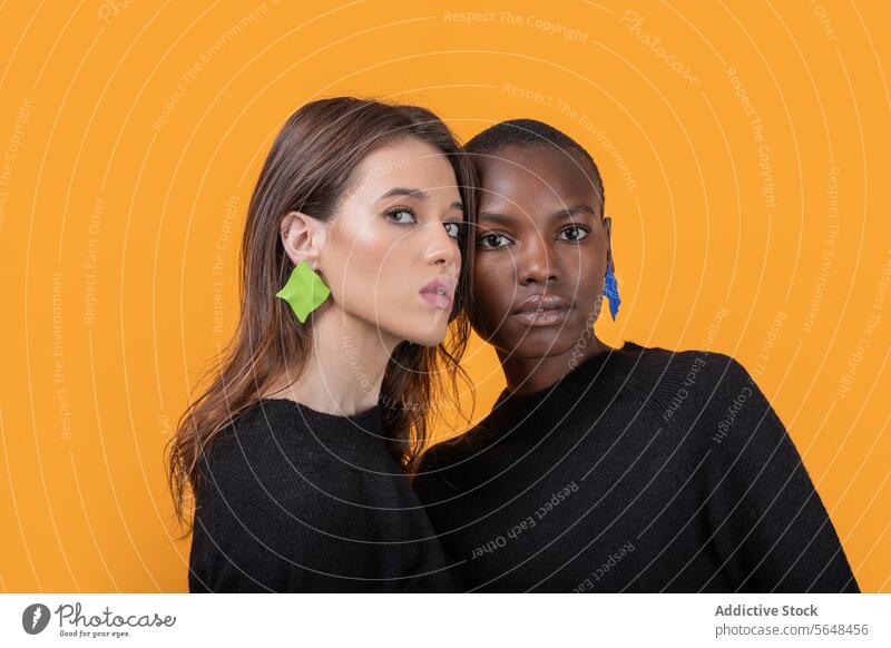 Diverse young female friends wearing colorful earrings embracing each other against yellow background women diverse confident portrait trendy tshirt together