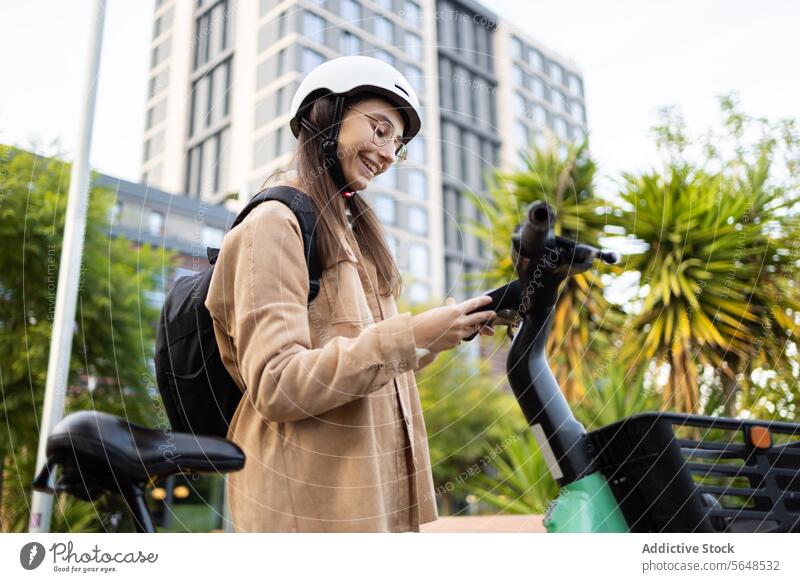 Young woman with helmet using smartphone on city e-scooter electric scooter urban casual wear smiling standing young technology transportation mobile app rental