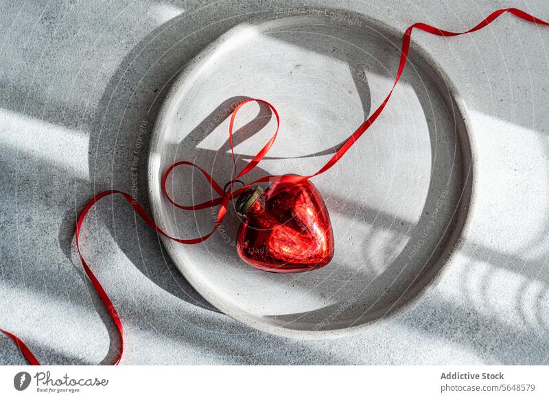 Top view of red heart ornament placed on plate on gray surface hand red ribbon concrete plate texture dynamic affection soft light tender romantic shiny rough