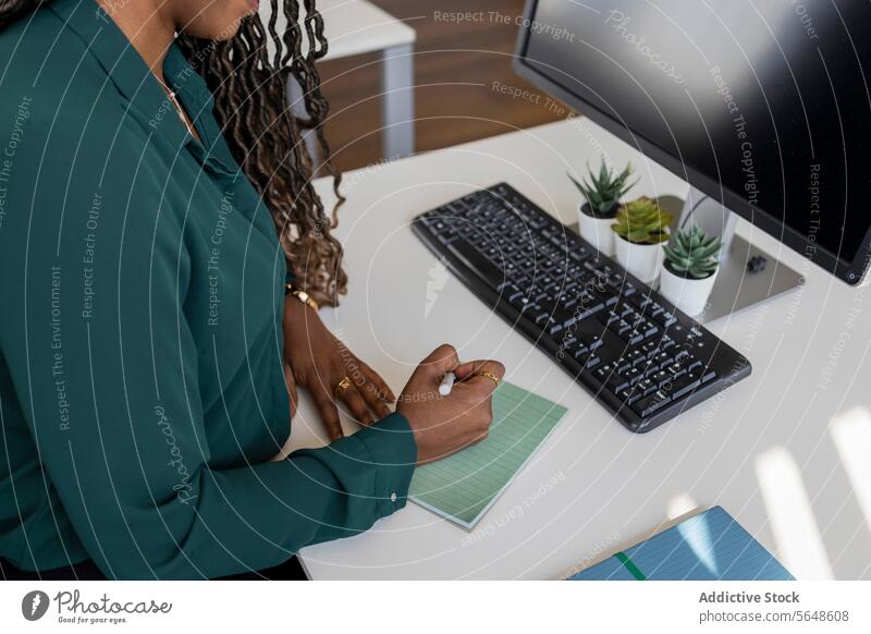 From above of young African American businesswoman writing on notepad at computer desk in office Businesswoman Write Notepad Desk Computer Keyboard From Above