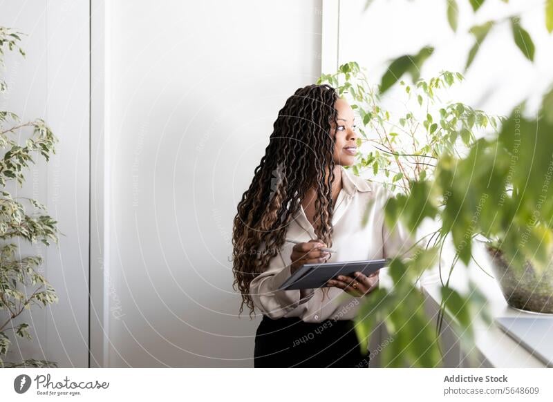 Thoughtful businesswoman holding digital tablet and stylus in office Businesswoman Office Digital Tablet Stylus Looking Through Window Professional Pensive