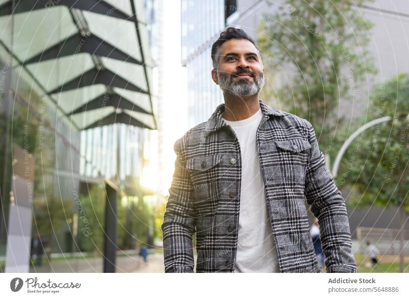 Smiling Indian businessman in casual outfit walking along street indian stroll smile happy daytime male city sidewalk positive optimist urban smart casual